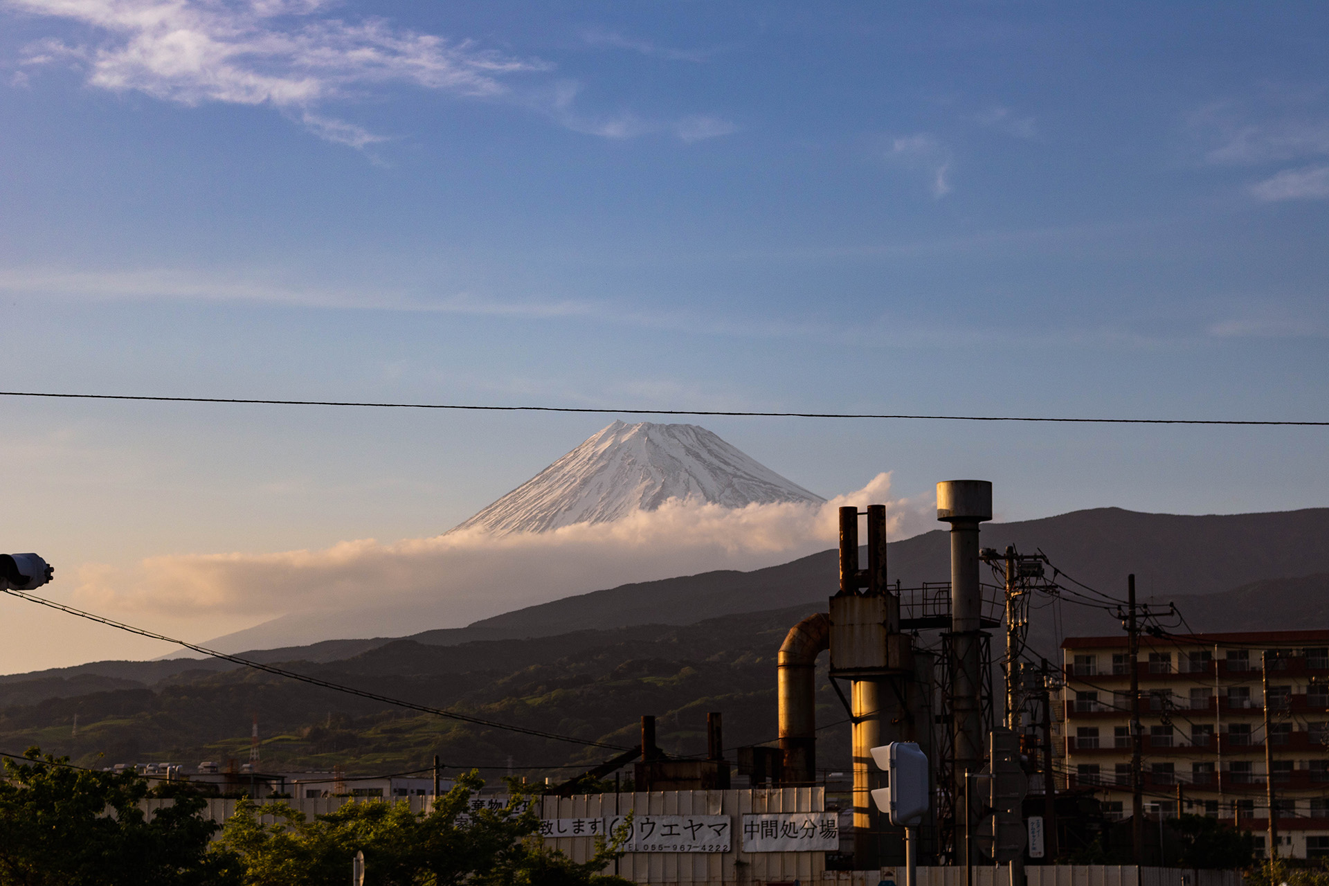 Golden hour view of Mount Fuji with snow at its peak and clouds covering its base.